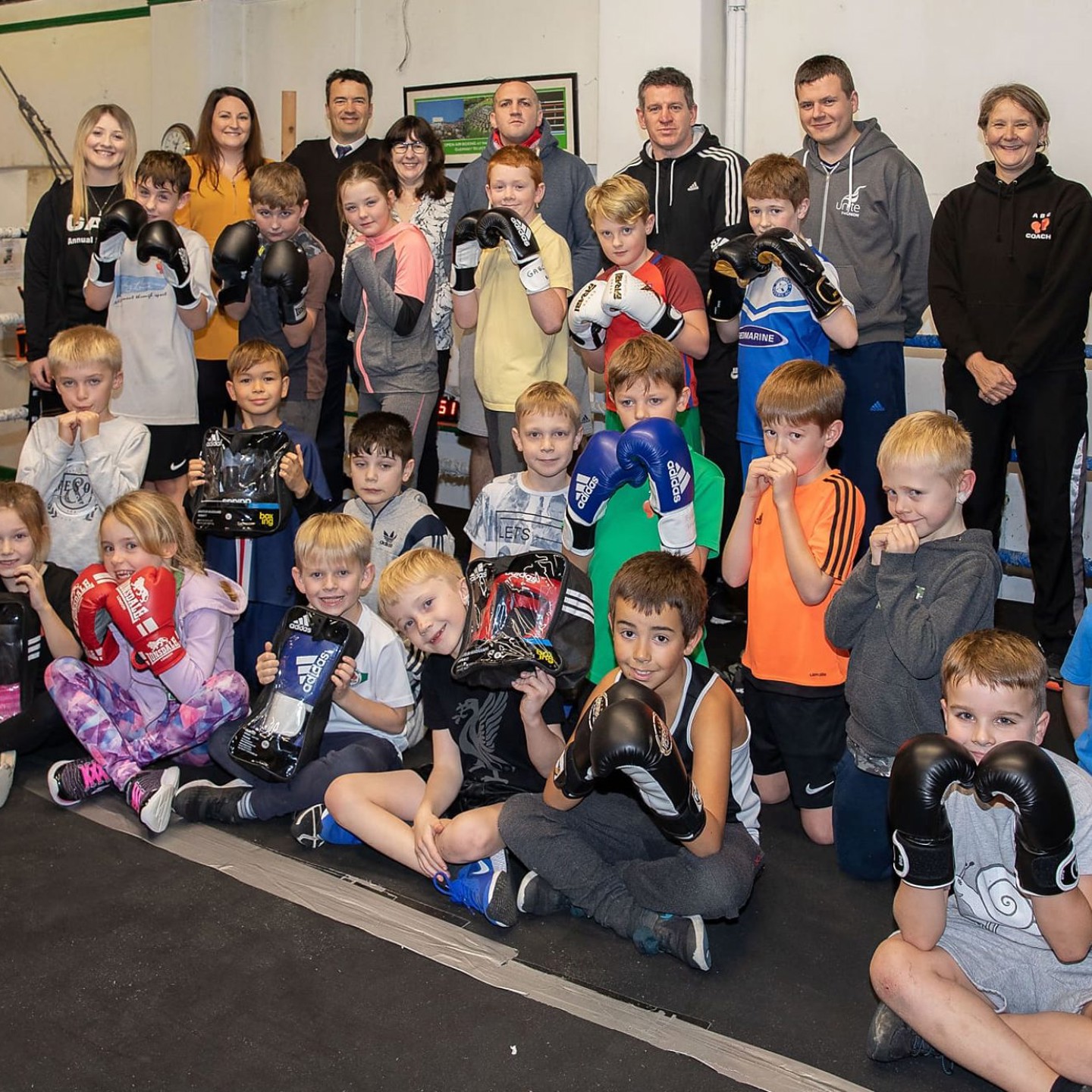 A group of children sitting in a boxing ring with gloves on posing for the camera