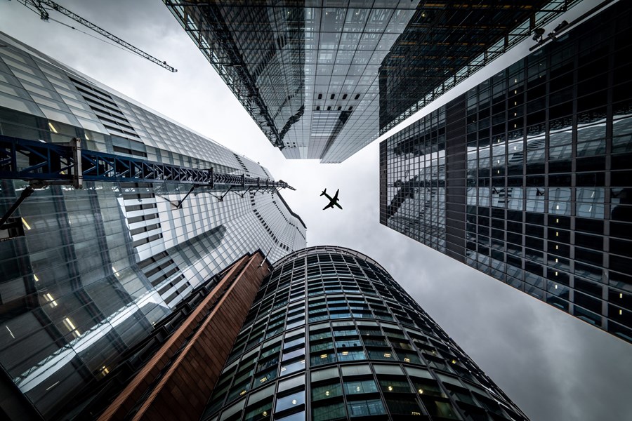An image of sky scrapers from the ground upwards, a plane is flying past also.
