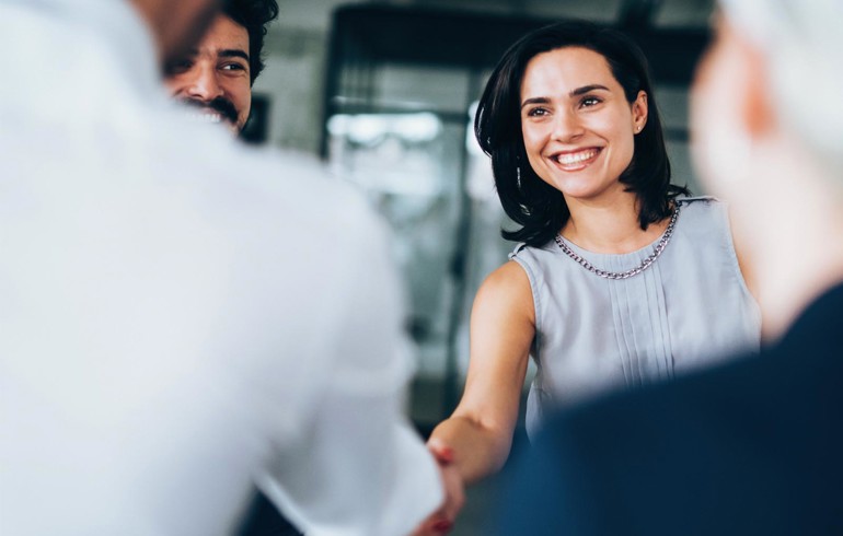 An image of a woman smiling while shaking a gentleman's hand