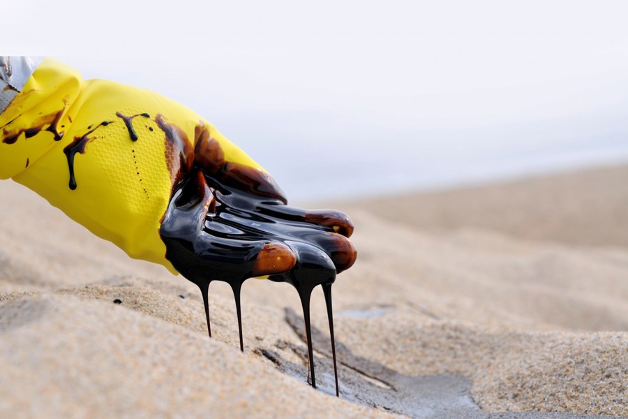 A yellow glove holding a handful of oil over sand