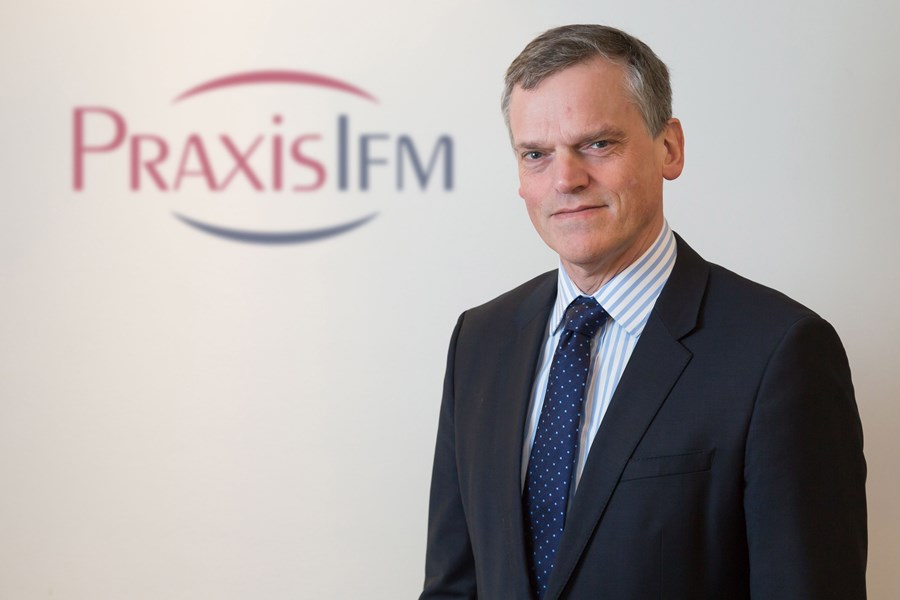 Simon Thornton standing in front of the Praxis IFM logo