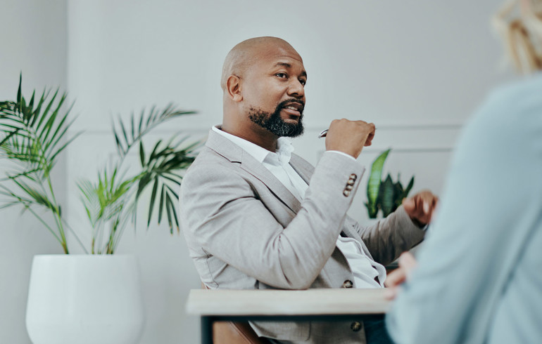 A man in a suit sat at a table having a conversation with a lady wearing blue