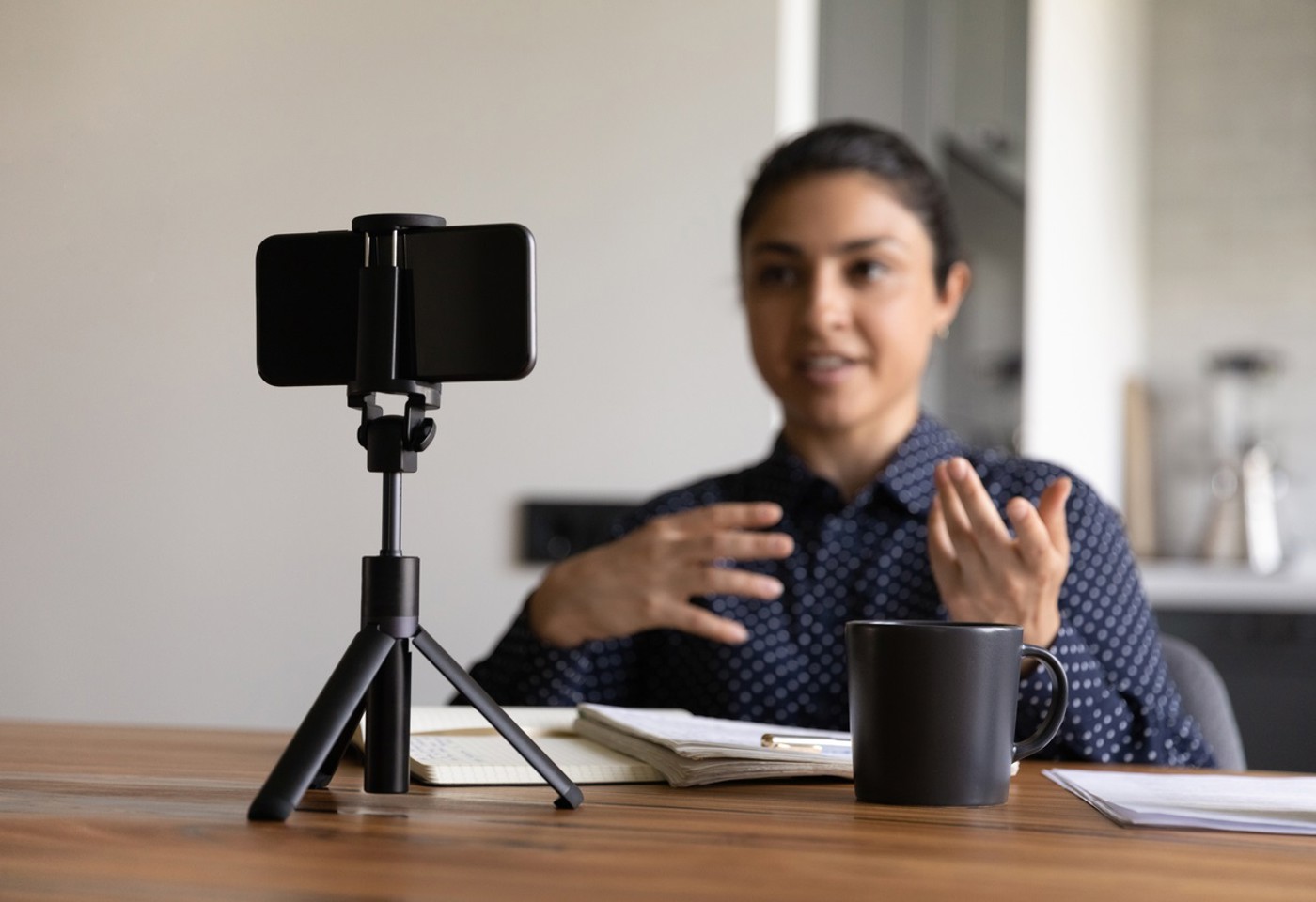Millennial Indian female vlogger or coach recording or video live broadcast on smartphone at home