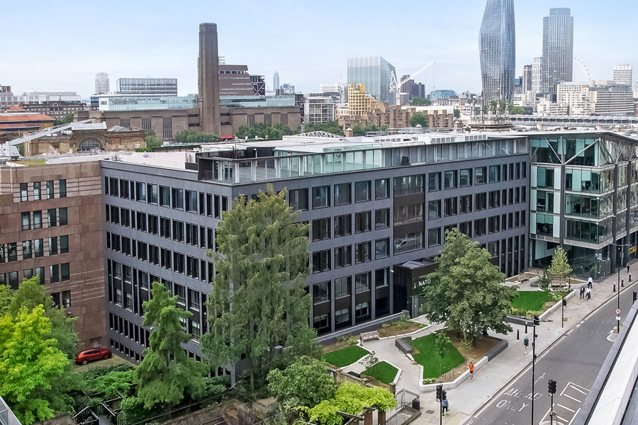 The London Praxis office, Senator house. A modern grey building with lots of windows. It's located next to a main road and there is many London skyscrapers in the background.