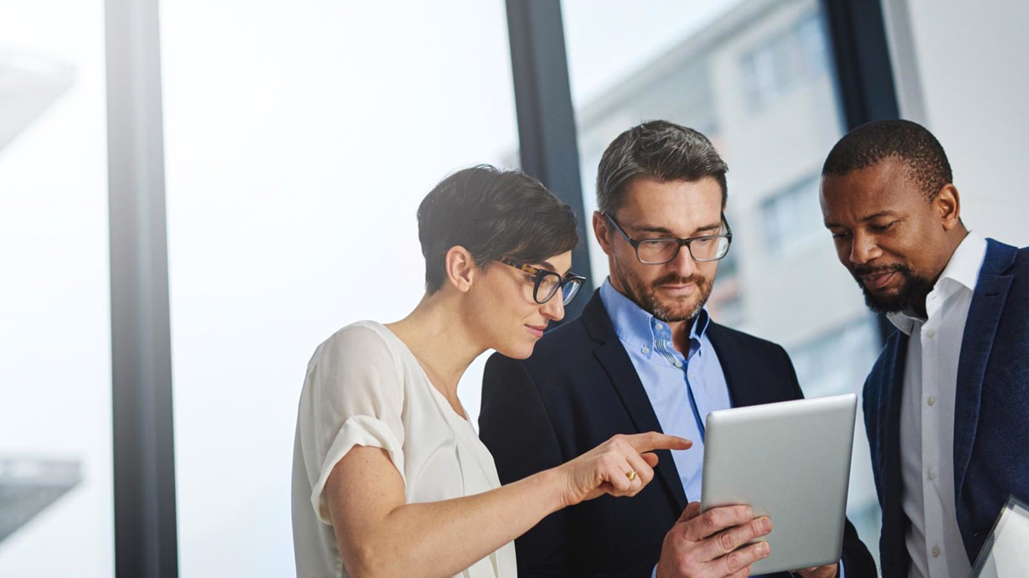 Two men and a woman in an office discussing using a hand held device