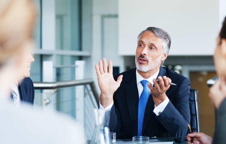 A middle-aged gentleman wearing a blue suit having an in-depth discussion during a meeting