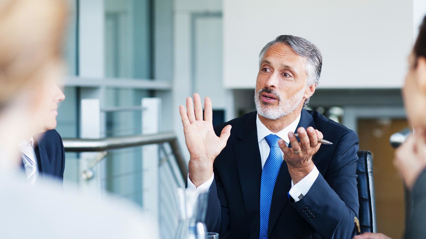 A middle-aged gentleman wearing a blue suit having an in-depth discussion during a meeting
