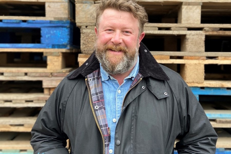 Mike Harris posing with his hands in his pockets in front of a stack of wooden crates. 
