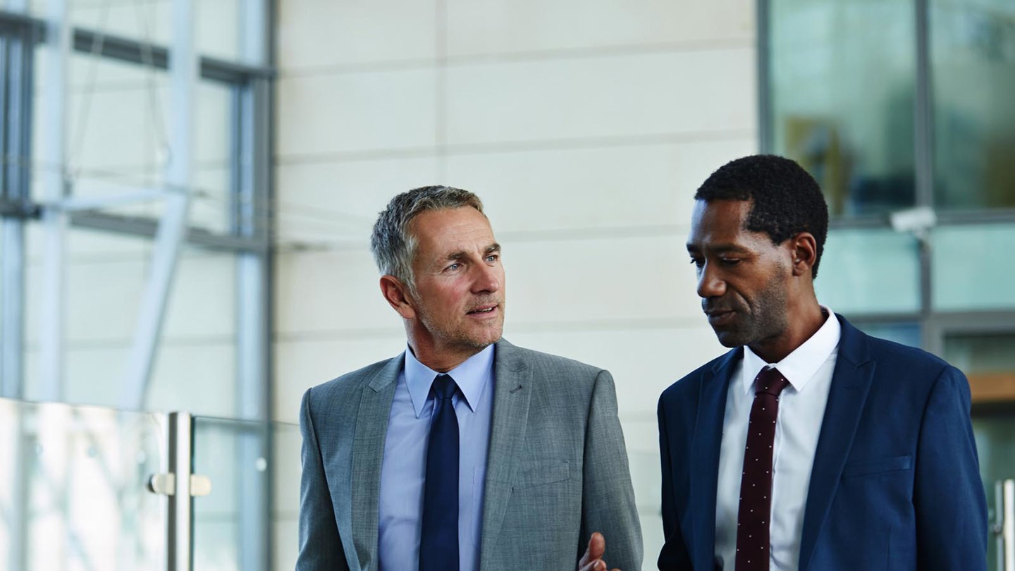 Two gentlemen in suits having a discussion while walking through an office