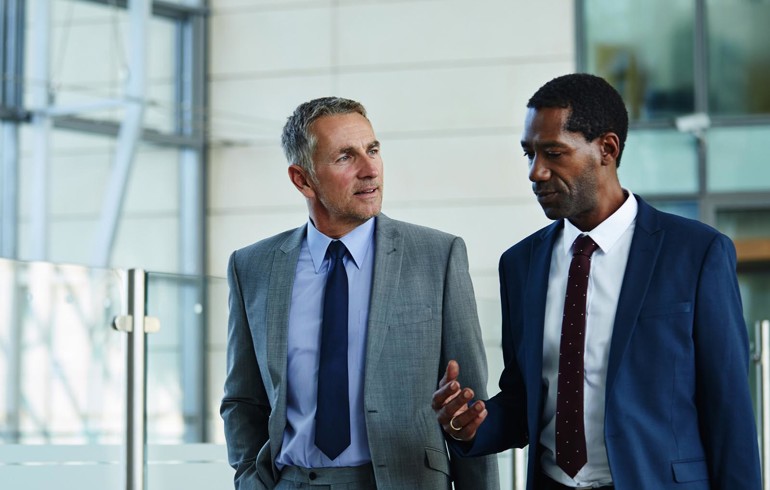 Two gentlemen in suits having a discussion while walking through an office
