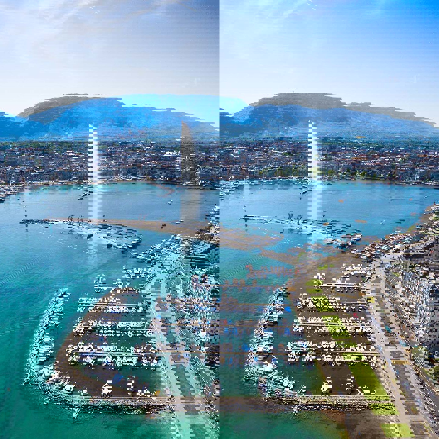 An image of  habour with a busy road next to it. There is a fountain in the distance