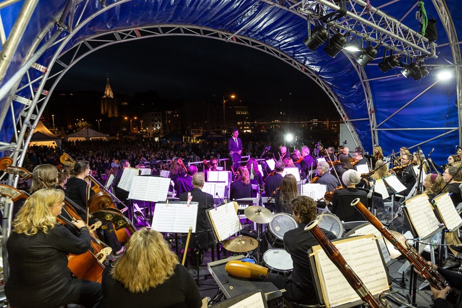 An orchestra performing on stage to a large crowd