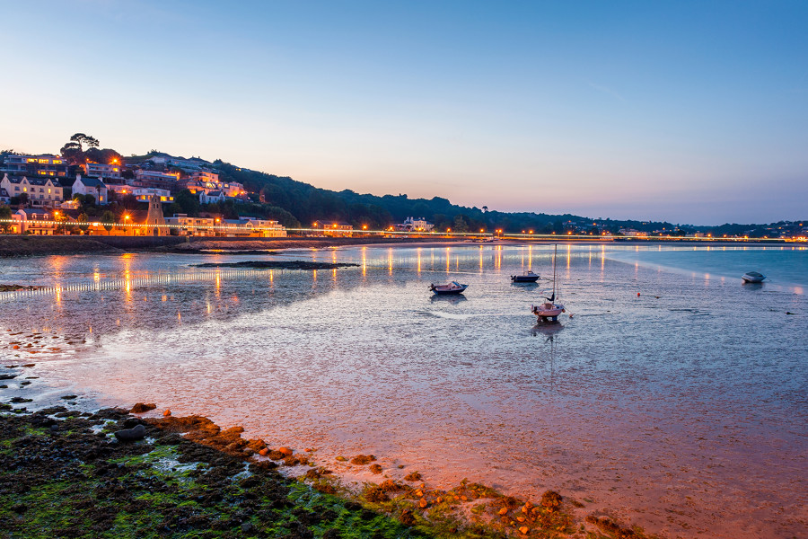 A view of the Jersey coast/beach while the sun is setting. The tide is low and the lights along the seafront are lit.