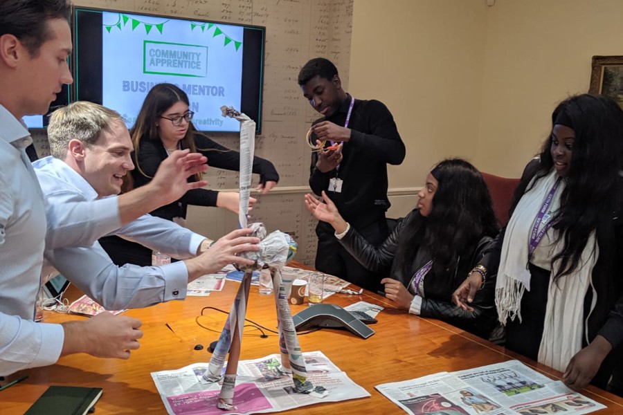 A diverse group of young people using their teamwork skills to create a sculpture out of newspaper.