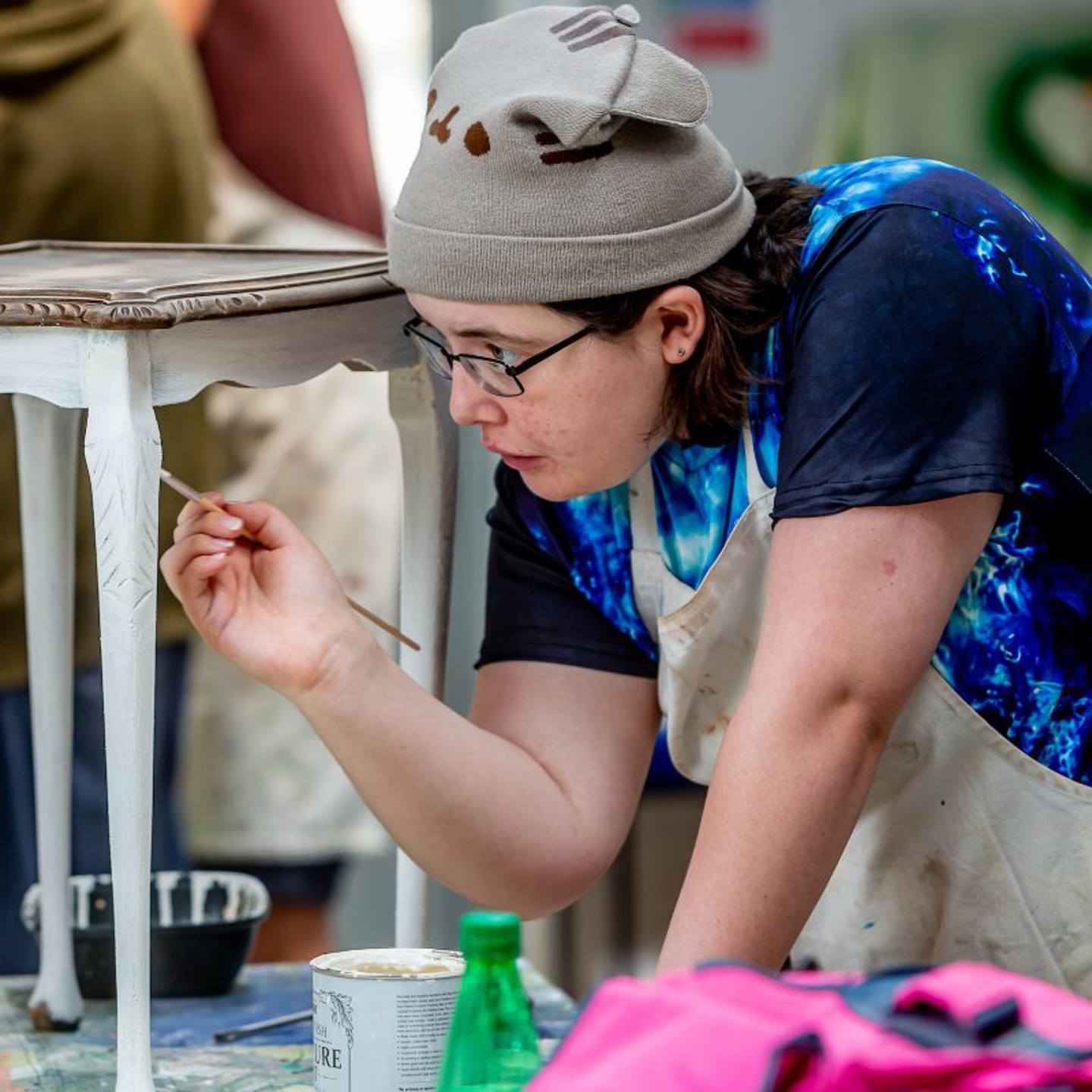 A woman wearing glasses painting a chair looking very concentrated 