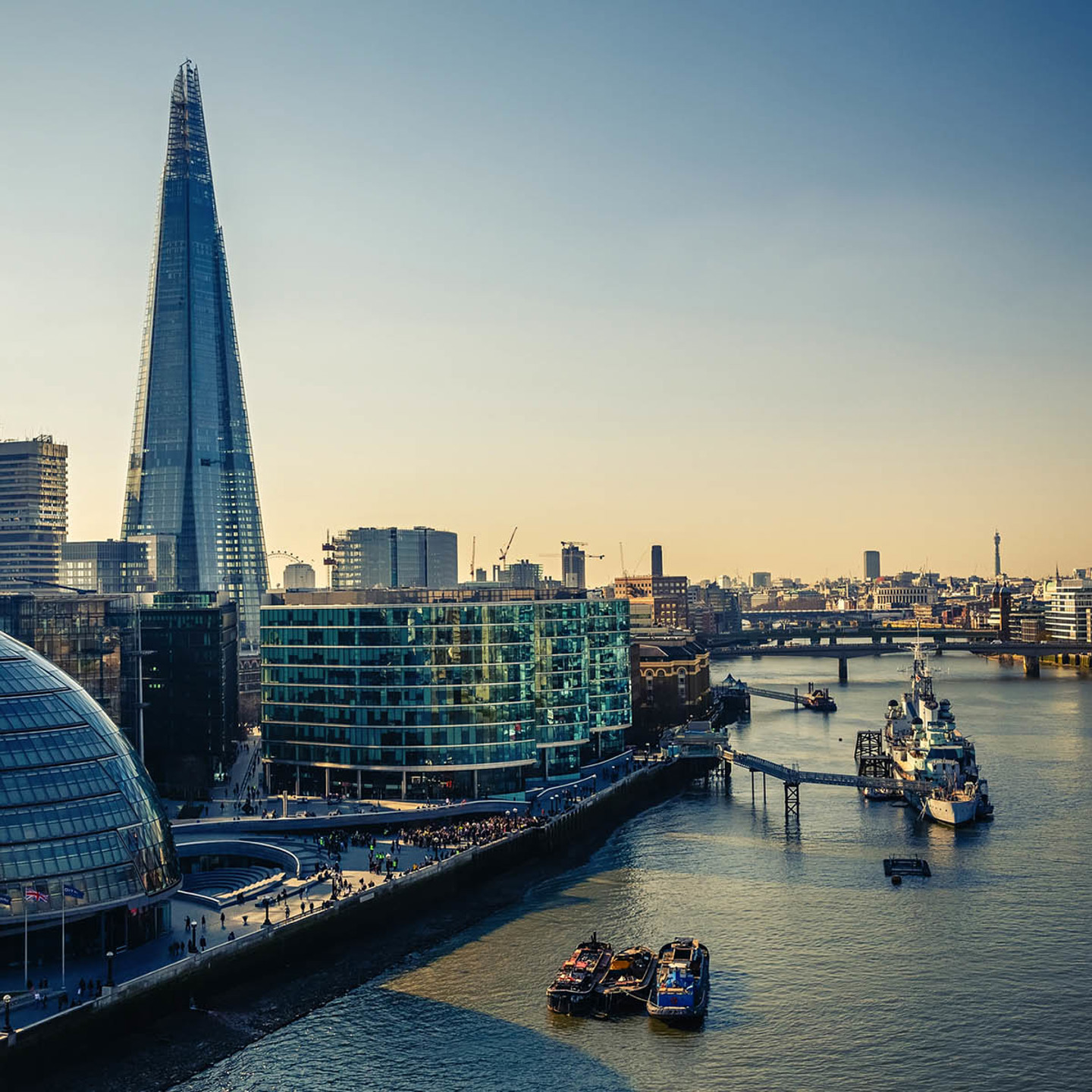 The River Thames with boats floating in it. Many modern London offices to the side of the river