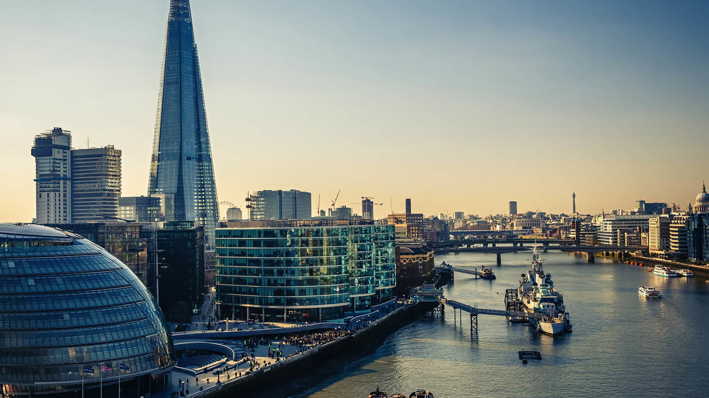 The River Thames with boats floating in it. Many modern London offices to the side of the river