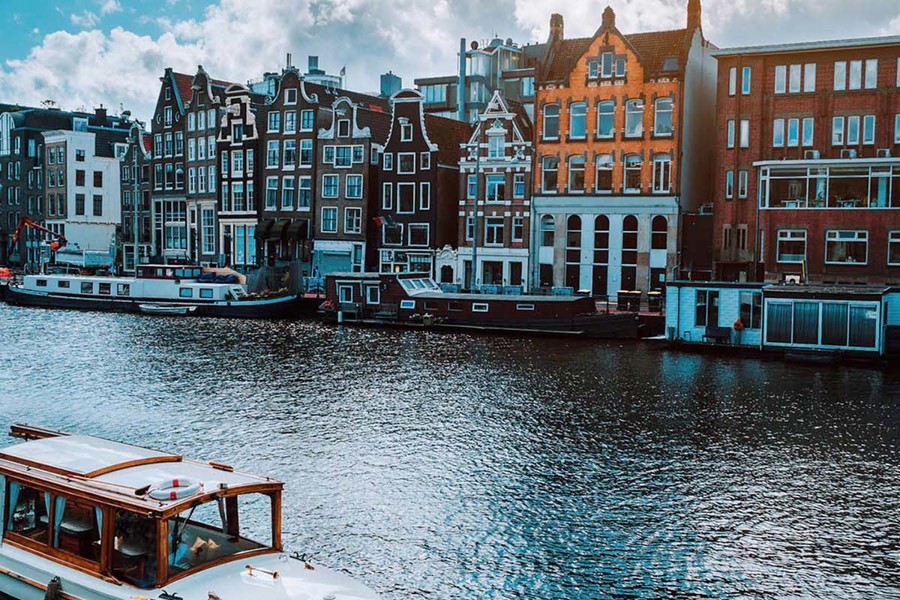 A river with many house boats floating through. Colourful buildings in the background.