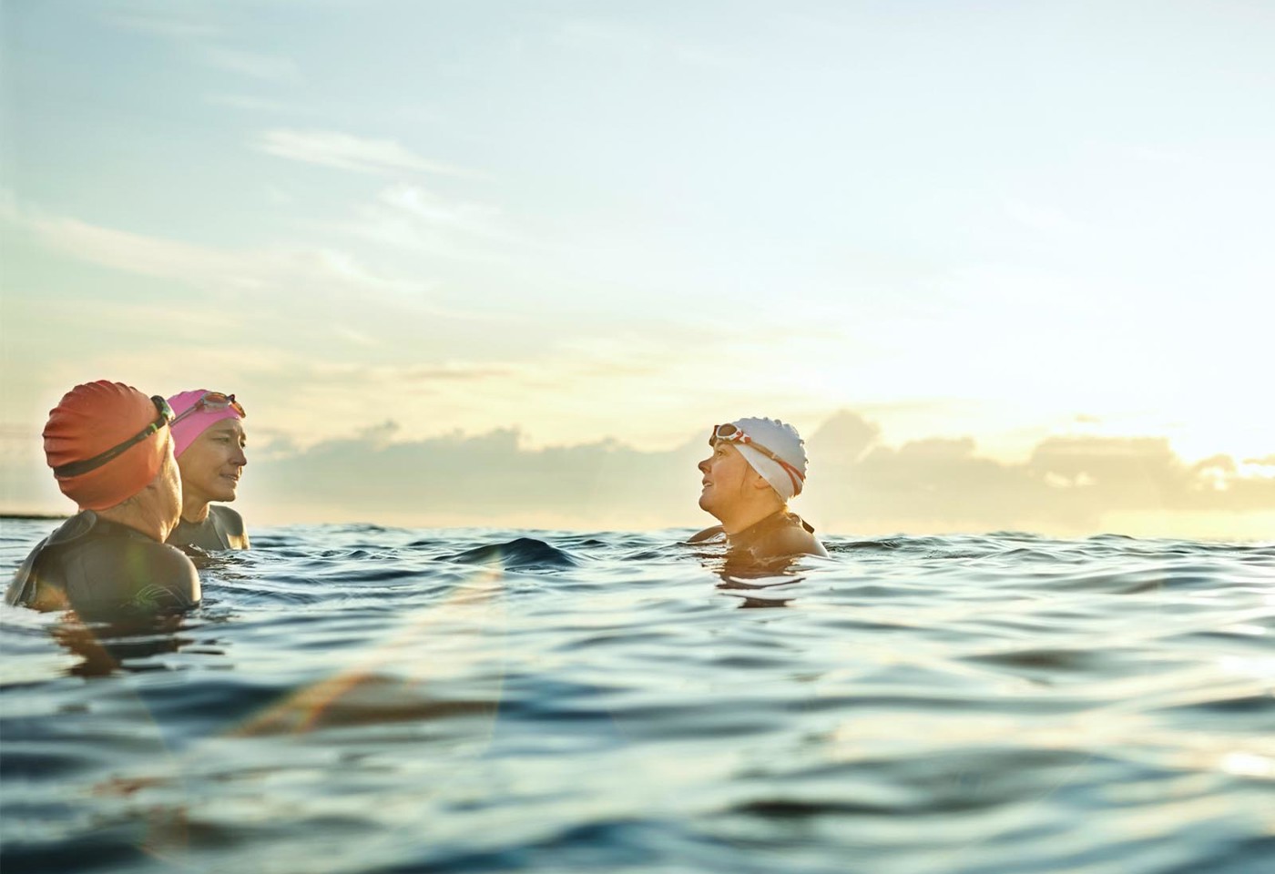3 swimmers wearing caps and goggles talking in the sea