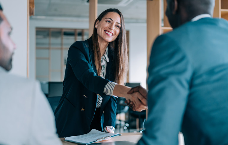 Womanleans Over Table To Shake Hands In A Meeting