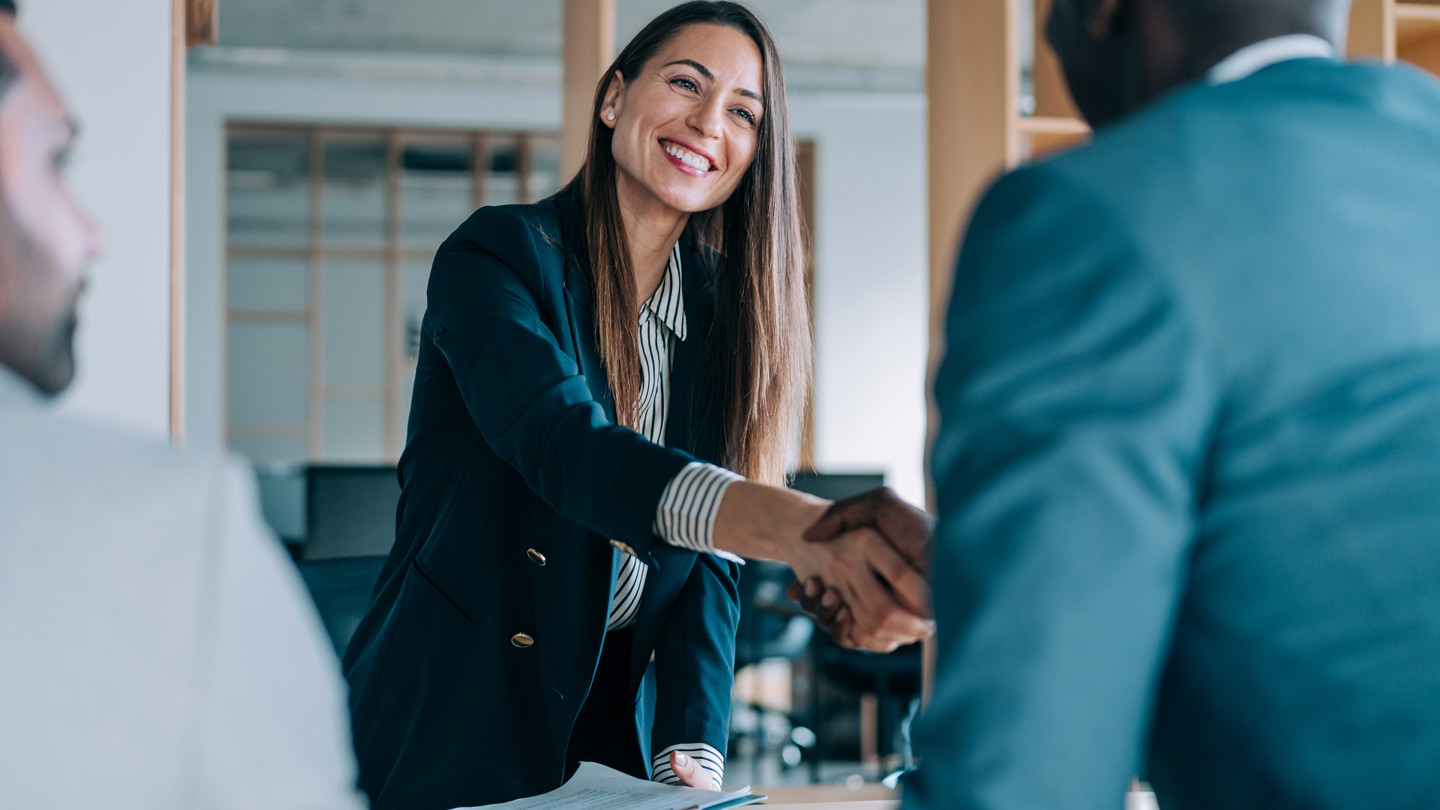 Womanleans Over Table To Shake Hands In A Meeting