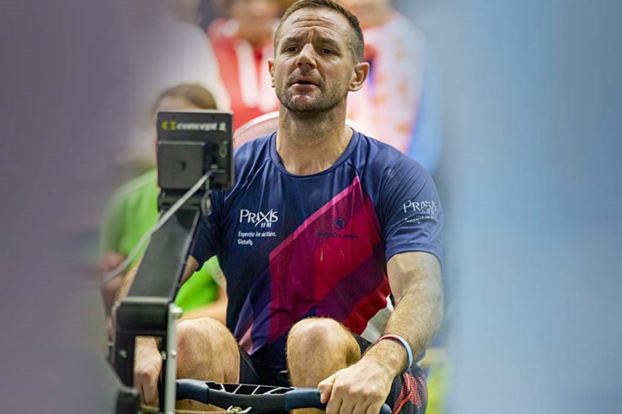 Simon Johns on a rowing machine for charity event sponsored by PraxisIFM