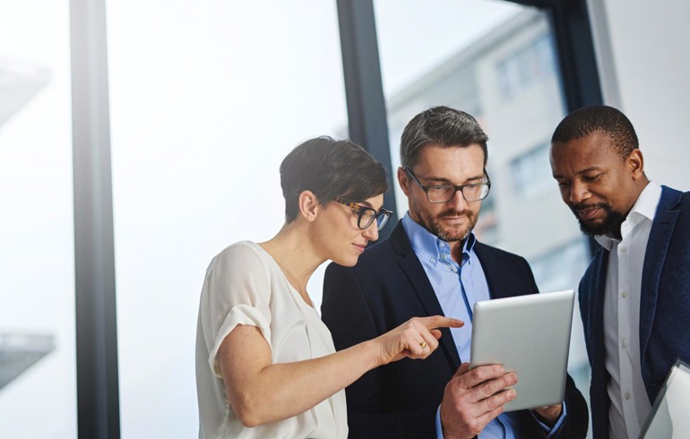 Two men and a woman in an office discussing using a hand held device 