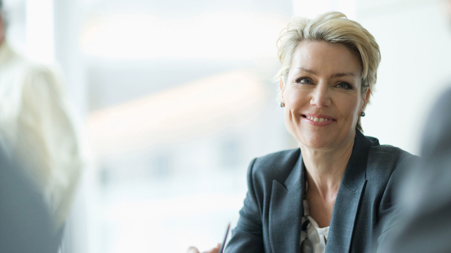 A blonde lady in a suit smiling at a colleague